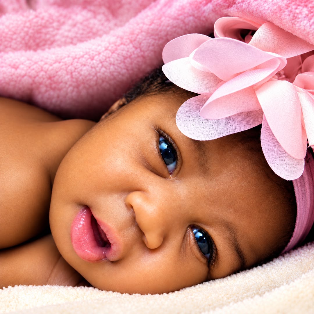 Alert newborn resting comfortably with a pink bow